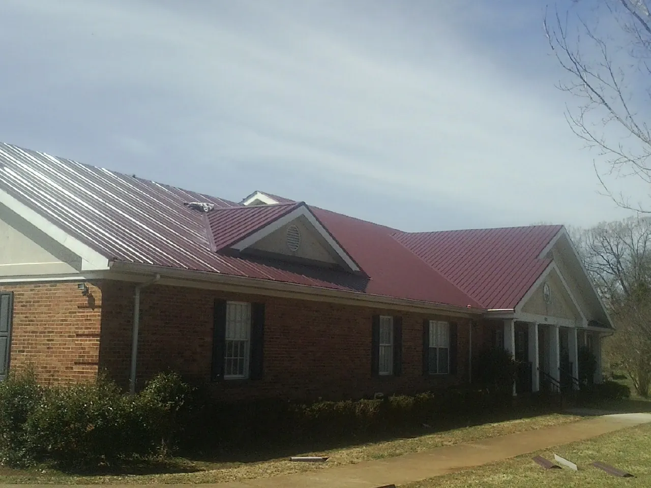 Red metal roof with gabled entries on a long brick building, from a Hail Damage Roof Repair job in Fairfax