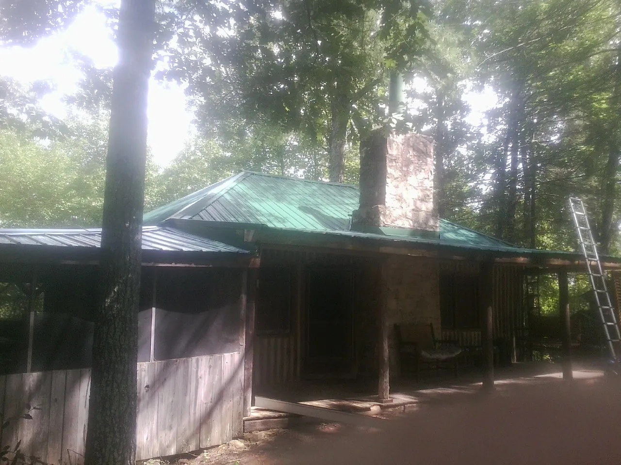 Green metal roof and stone chimney above a log cabin porch in Fairfax